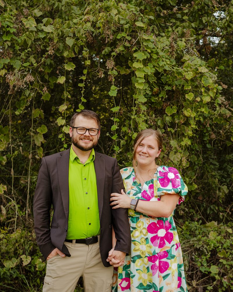 Me and my wife, smiling in front of a wall of green vines